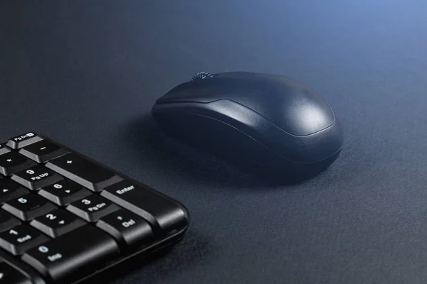 Wireless mouse with black keyboard on black surface. Glow