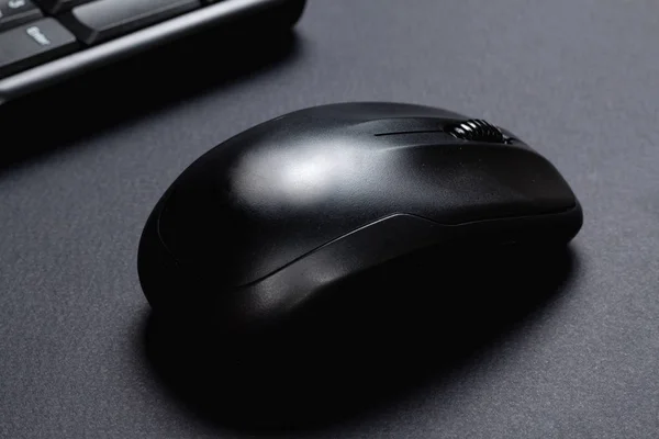 Wireless mouse with black keyboard on black surface.