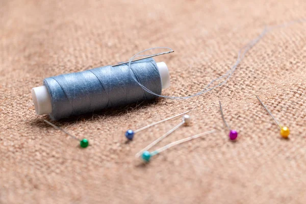 Coil thread with a needle stuck in it next to the tailor pins on the burlap.