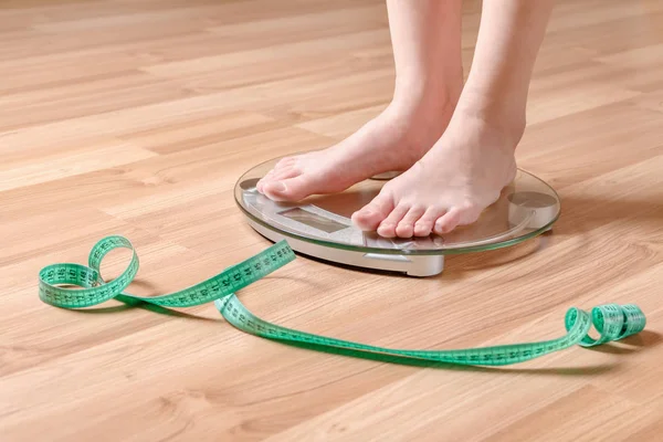 A girl stands on the scales next to the tape measure, check the weight.