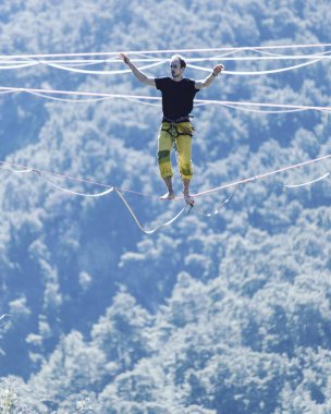Highliner ipte. Dağların arka planında yüksek bir çizgi. Doğada ekstrem bir spor. Askıda dengede duruyor. İrtifada denge.