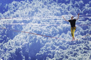 Highliner ipte. Dağların arka planında yüksek bir çizgi. Doğada ekstrem bir spor. Askıda dengede duruyor. İrtifada denge.