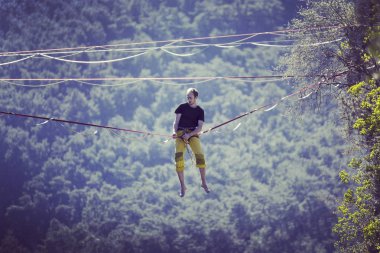 Highliner ipte. Dağların arka planında yüksek bir çizgi. Doğada ekstrem bir spor. Askıda dengede duruyor. İrtifada denge.