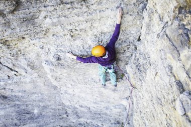 Adam dağcı. Kaya tırmanışçısı kayalık bir duvara tırmanıyor. Adam sert hareket yapar.