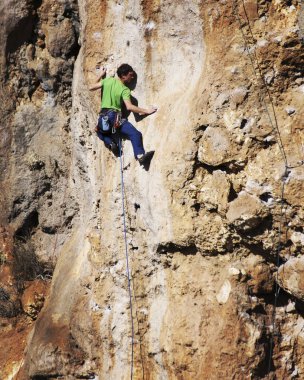 Adam dağcı. Kaya tırmanışçısı kayalık bir duvara tırmanıyor. Adam sert hareket yapar.
