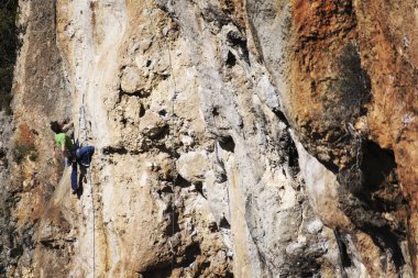 Adam dağcı. Kaya tırmanışçısı kayalık bir duvara tırmanıyor. Adam sert hareket yapar.