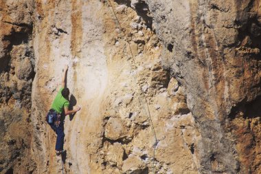 Adam dağcı. Kaya tırmanışçısı kayalık bir duvara tırmanıyor. Adam sert hareket yapar.