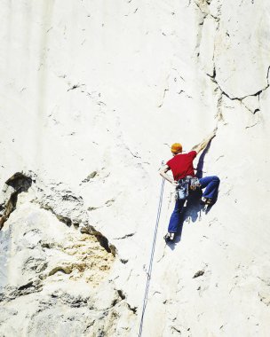 Genç adam uçurumun üzerinde zorlu rota tırmanma sırasında ararken.