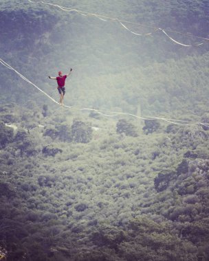 Highliner ipte. Dağların arka planında yüksek bir çizgi. Doğada ekstrem bir spor. Askıda dengede duruyor. İrtifada denge.