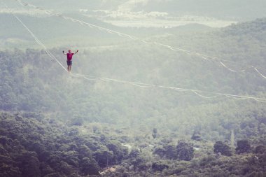 Highliner ipte. Dağların arka planında yüksek bir çizgi. Doğada ekstrem bir spor. Askıda dengede duruyor. İrtifada denge.