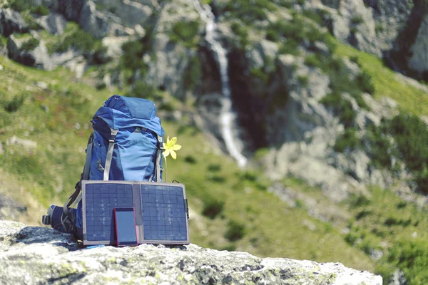 The backpack stands on a trail in the background of the mountains. The sun panel hangs on the backpack.
