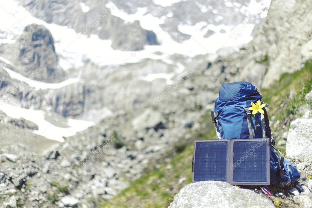 The backpack stands on a trail in the background of the mountains. The sun panel hangs on the backpack.