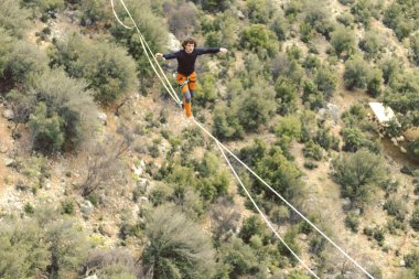 Highliner ipte. Dağların arka planında yüksek bir çizgi. Doğada ekstrem bir spor. Askıda dengede duruyor. İrtifada denge.