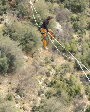 Highliner ipte. Dağların arka planında yüksek bir çizgi. Doğada ekstrem bir spor. Askıda dengede duruyor. İrtifada denge.