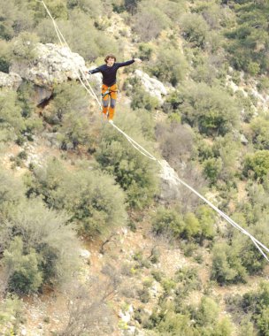 Highliner ipte. Dağların arka planında yüksek bir çizgi. Doğada ekstrem bir spor. Askıda dengede duruyor. İrtifada denge.