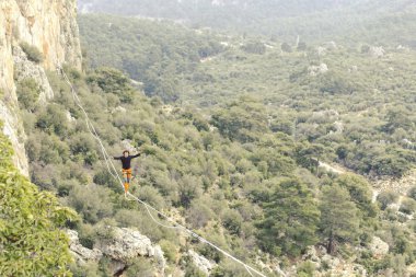 Highliner ipte. Dağların arka planında yüksek bir çizgi. Doğada ekstrem bir spor. Askıda dengede duruyor. İrtifada denge.