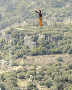 Highliner ipte. Dağların arka planında yüksek bir çizgi. Doğada ekstrem bir spor. Askıda dengede duruyor. İrtifada denge.