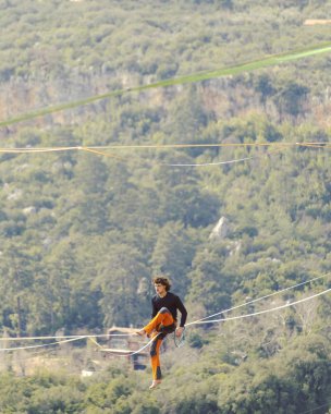 Highliner ipte. Dağların arka planında yüksek bir çizgi. Doğada ekstrem bir spor. Askıda dengede duruyor. İrtifada denge.