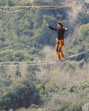 Highliner ipte. Dağların arka planında yüksek bir çizgi. Doğada ekstrem bir spor. Askıda dengede duruyor. İrtifada denge.
