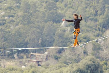 Highliner ipte. Dağların arka planında yüksek bir çizgi. Doğada ekstrem bir spor. Askıda dengede duruyor. İrtifada denge.