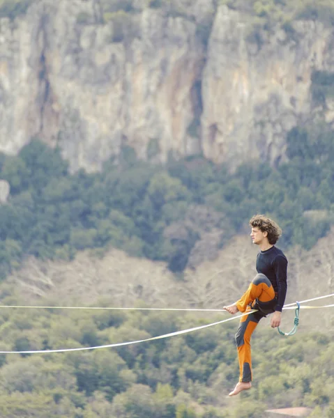 Highliner ipte. Dağların arka planında yüksek bir çizgi. Doğada ekstrem bir spor. Askıda dengede duruyor. İrtifada denge.