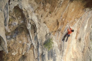 Adam dağcı. Kaya tırmanışçısı kayalık bir duvara tırmanıyor. Adam sert hareket yapar.