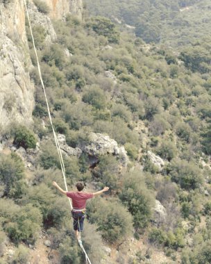 Highliner ipte. Dağların arka planında yüksek bir çizgi. Doğada ekstrem bir spor. Askıda dengede duruyor. İrtifada denge.