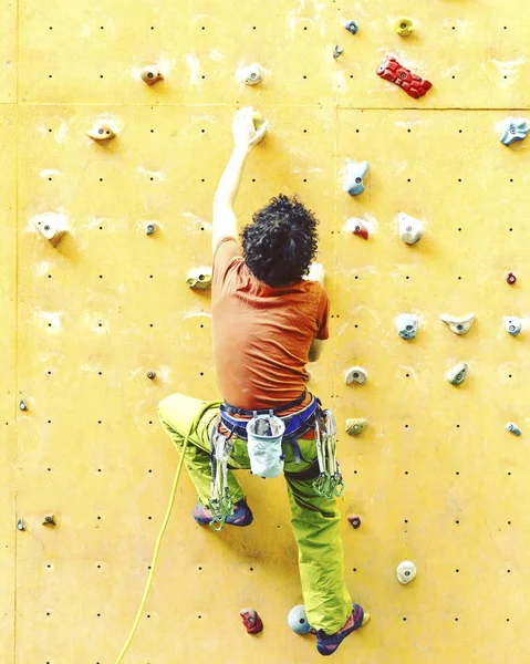 Man bouldering at an indoor climbing centre. Climber practicing rock climbing at an indoor climbing gym.