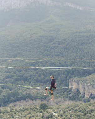 Highliner ipte. Dağların arka planında yüksek bir çizgi. Doğada ekstrem bir spor. Askıda dengede duruyor. İrtifada denge.