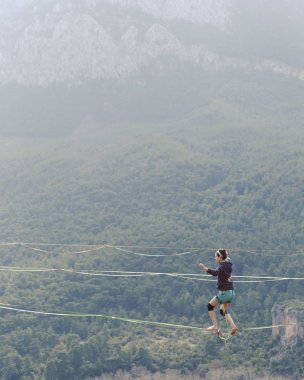 Highliner ipte. Dağların arka planında yüksek bir çizgi. Doğada ekstrem bir spor. Askıda dengede duruyor. İrtifada denge.