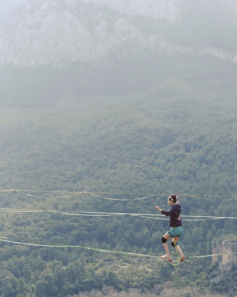 Highliner ipte. Dağların arka planında yüksek bir çizgi. Doğada ekstrem bir spor. Askıda dengede duruyor. İrtifada denge.