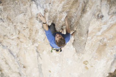 Genç adam uçurumun üzerinde zorlu rota tırmanma sırasında ararken.