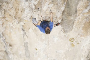 Genç adam uçurumun üzerinde zorlu rota tırmanma sırasında ararken.