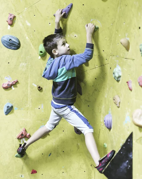 Little boy climbing a rock wall indoor. Concept of sport life.