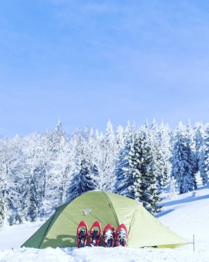 Dağlarda kış yürüyüş. Çadırın yakınında karda kar ayakkabıları vardır.