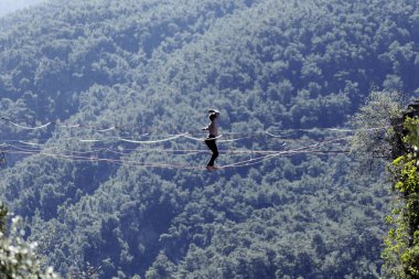 Highliner ipte. Dağların arka planında yüksek bir çizgi. Doğada ekstrem bir spor. Askıda dengede duruyor. İrtifada denge.