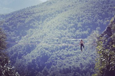 Highliner ipte. Dağların arka planında yüksek bir çizgi. Doğada ekstrem bir spor. Askıda dengede duruyor. İrtifada denge.