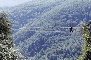 Highliner ipte. Dağların arka planında yüksek bir çizgi. Doğada ekstrem bir spor. Askıda dengede duruyor. İrtifada denge.