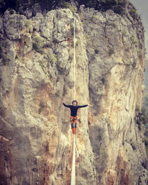 Highliner ipte. Dağların arka planında yüksek bir çizgi. Doğada ekstrem bir spor. Askıda dengede duruyor. İrtifada denge.