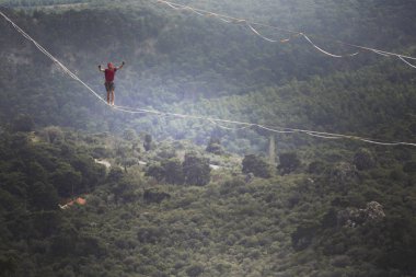 Highliner ipte. Dağların arka planında yüksek bir çizgi. Doğada ekstrem bir spor. Askıda dengede duruyor. İrtifada denge.