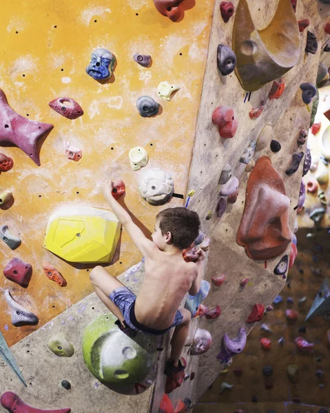 Little boy climbing a rock wall indoor.