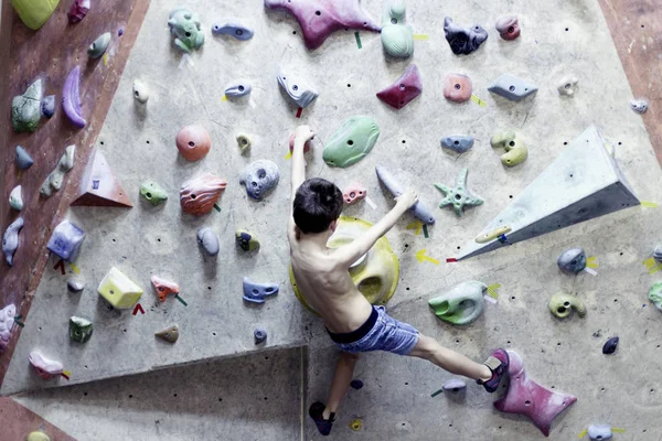 Little boy climbing a rock wall indoor.