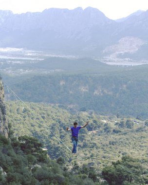 Bir adam gergin bir sapan boyunca yürüyor. Mounta Highline