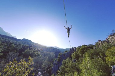 Bir adam gergin bir sapan boyunca yürüyor. Mounta Highline