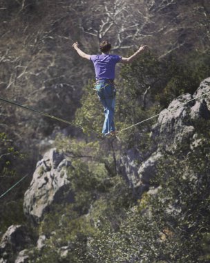Bir adam gergin bir sapan boyunca yürüyor. Mounta Highline