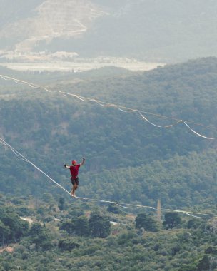 Bir adam gerilmiş askı boyunca yürüyor. Dağlarda yüksek bir yer. İnsan dengeyi yakalar. Doğada bir ip cambazının performansı. Vadinin arka planındaki dağcı..