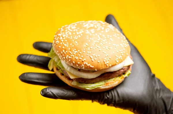 burger in hand in a black glove on a yellow background