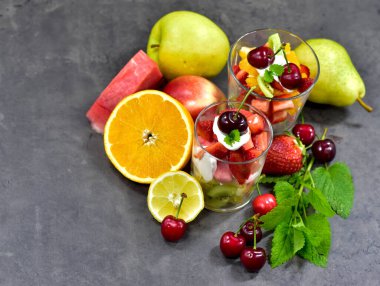 Vitaminler, meyve kokteyli, 2 bardak doğranmış meyve ve ahşap arka planda bir kiraz.