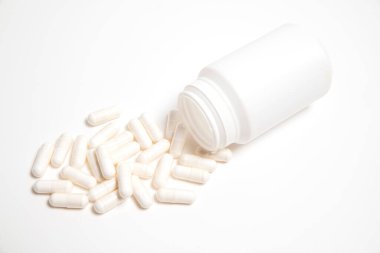 Beyaz arka planda hapların yazıları olmayan beyaz plastik tüp ve yanında beyaz haplar.