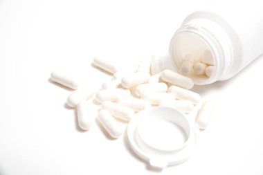 Beyaz arka planda hapların yazıları olmayan beyaz plastik tüp ve yanında beyaz haplar.